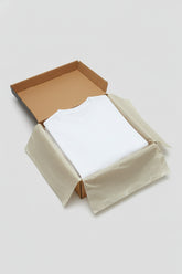 White premium cotton t-shirt neatly folded in a cardboard box with tissue paper.